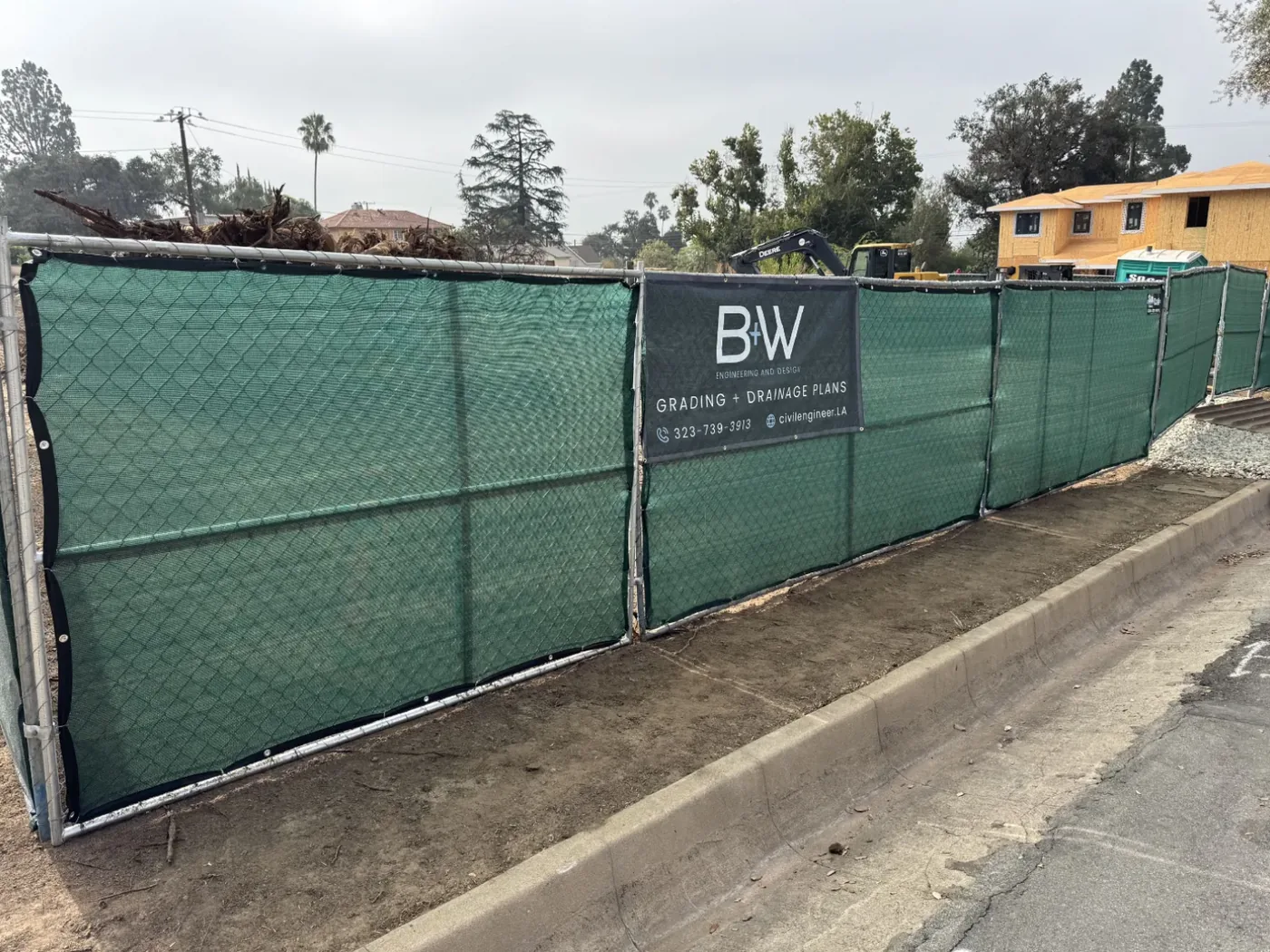 B+W banner mounted on green-screened construction fencing at a second Altadena site, with an excavator working behind it